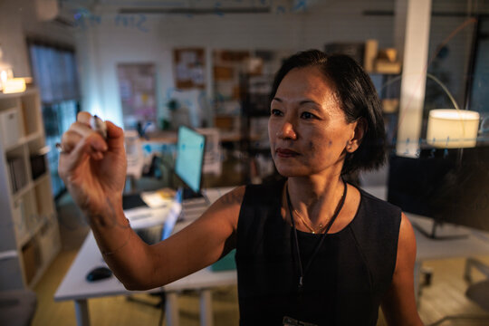 Woman writing on clear board in office setting.