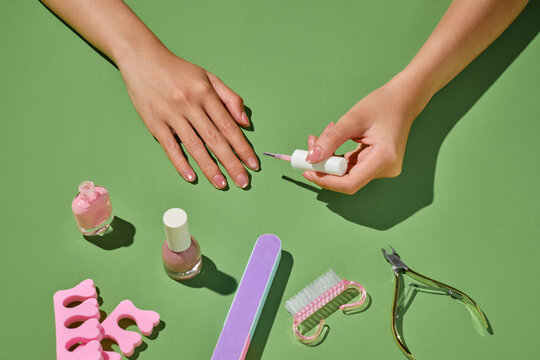 Hands applying nail polish on green background