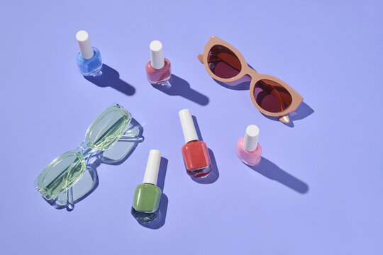 Stylish arrangement of nail polish bottles and sunglasses on purple