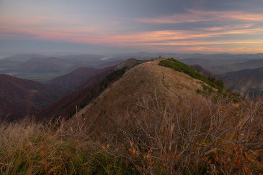 View of a golden ridge cresting against a pastel sky, with distant peaks fading into the horizon's embrace, Kraviarske, Mala Fatra, Zilina Region, Slovakia.
