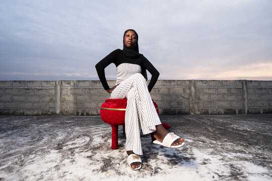 African woman wearing hijab sitting on rooftop at sunset