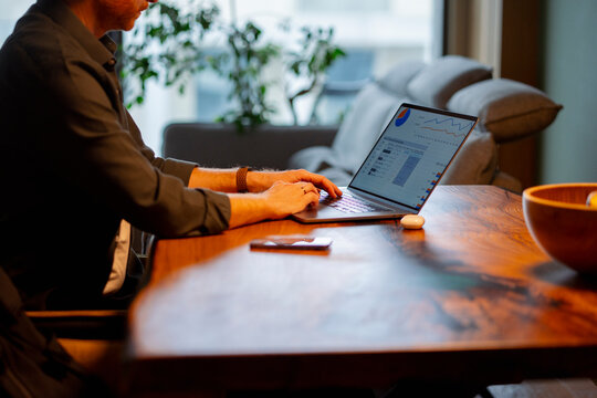 Person works on laptop at wooden table in bright room
