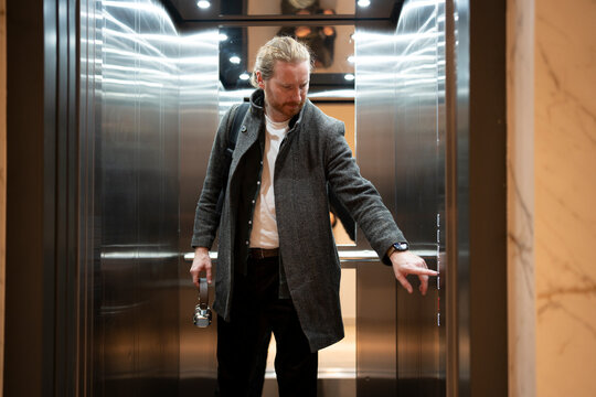 Man reaches for elevator button in modern building lobby
