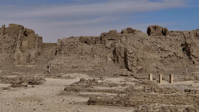 Medinet Habu temple mudbrick walls and fortification ruins in Luxor Egypt, ancient eroded defensive structures and residential quarters archaeological site under cloudy sky.