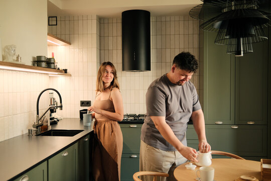 Happy couple making tea at the kitchen at home, talking to each other 