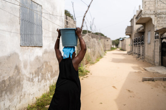African woman carrying water bucket on dusty village street