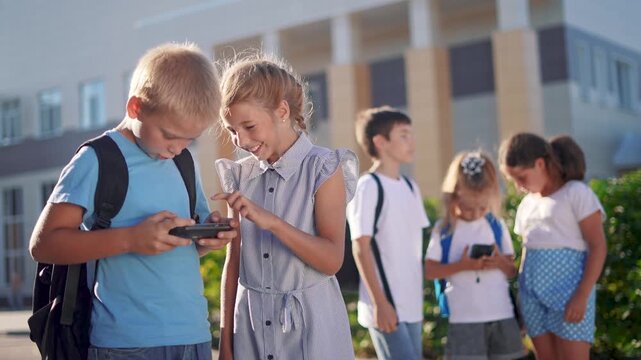 children group school children look lifestyle at the smartphone video. school learning kid concept. group of kids with backpacks playing smartphone near the school building outdoors