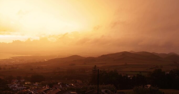 A beautiful sunset over a small town with houses and a hill at Capelas, Azores.
