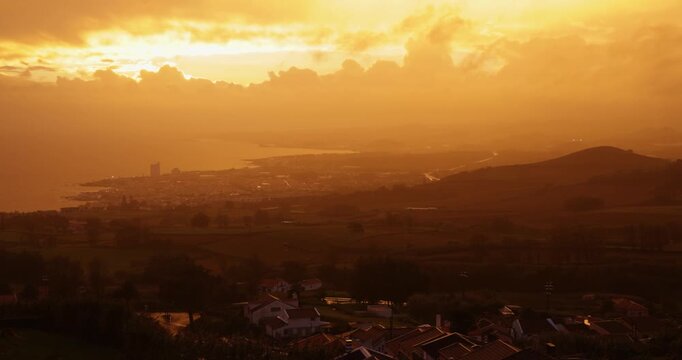 A beautiful sunset over a small town with houses and a hill at Capelas, Azores.