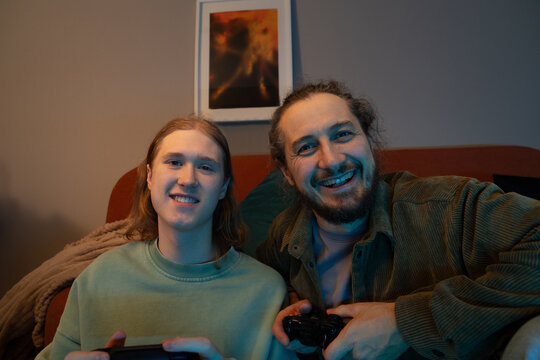 Father and son smiling while playing video games at home
