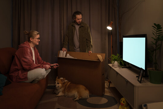 Couple unpacking new television in living room with dog