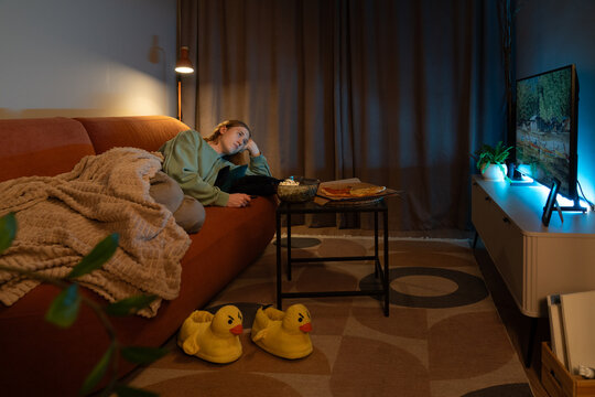 Young man lying on sofa watching TV show alone at night