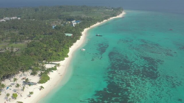 Wide aerial landscape of Thoddoo island coastline showing a long white sand beach, lush green palm forest, anchored boats, and expansive shallow turquoise water with coral reefs.