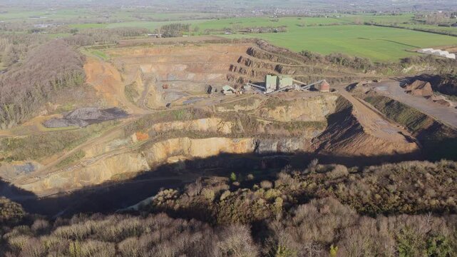 Aerial view of a quarry's contrasting textures and tones, with exposed rock faces and piles of earth, surrounded by green fields, La Roche-Jaudy, France.