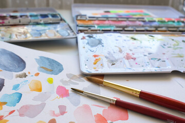 Watercolor artist workspace  view of paint brushes, colorful palette, and abstract sketches on paper