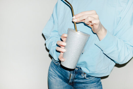 Person holding sparkly silver shiny party drink cup and straw 