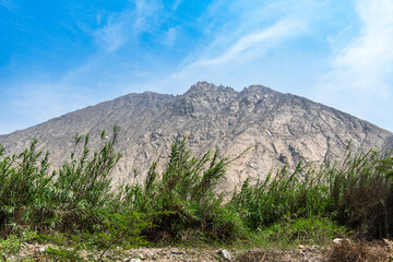 Fototapeta premium Large sunlit mountain rising above the lush green valley of Cieneguilla, Lima, Peru.