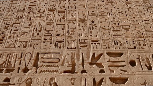 Closeup of ancient Egyptian hieroglyphic inscriptions with cartouches and bird symbols carved in sandstone wall at Medinet Habu temple in Luxor Egypt, detailed royal text. 