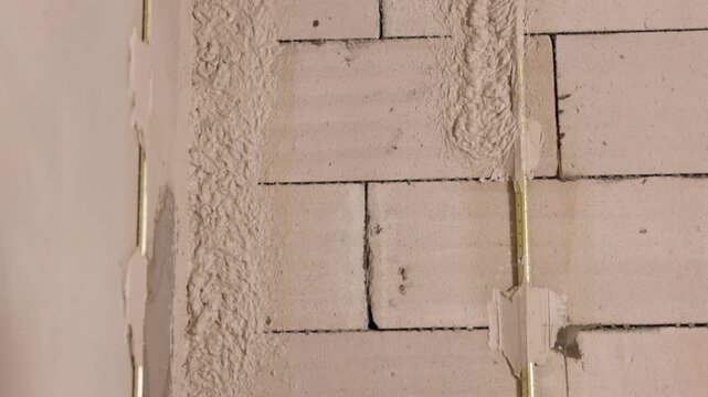 Applying plaster, Plaster hose, Wall repair. Close-up view spray hose applying wet plaster texture to interior cinder block wall during renovation and insulation work.