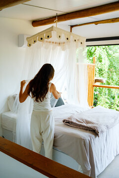 Woman Adjusting Bed Canopy in Cozy Room