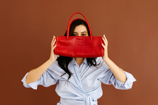 Woman holding red leather handbag covering face