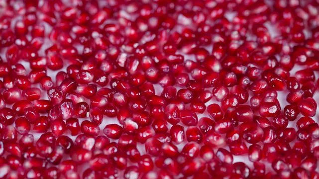 Vivid pomegranate imagery. Bright red pomegranate seeds with glossy translucent skins. Intimate closeup showcasing sparkling ruby seeds against simple studio background