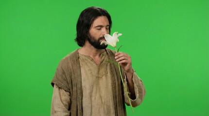 Naklejka premium Man with long hair and beard in ancient garment smelling a white lily flower. Religious portrait with spiritual significance for Easter.