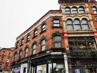 Naklejka premium Historic brick building facade on a Manchester street with shopfronts and pedestrians