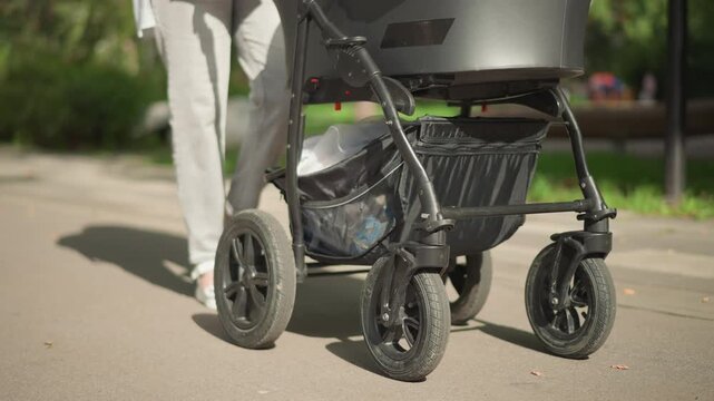 Lowangle white parent pushing stroller wheels along park pavement, closeup of robust wheel suspension rolling over sunlit pathway, modern stroller design showcased, product mobility test, confident