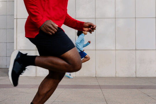 Lower body of fit man in the foreground with another runner behind him
