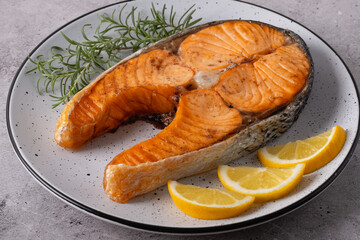 Seared salmon steak with rosemary and lemon pieces on grey table