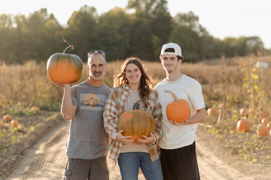 A portrait of a father and his two children having fun at a  pumpkin patch