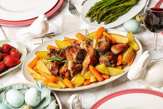 Homemade Easter dinner. Oval plate with Oven roasted Lamb with Carrots & Potatoes. Asparagus, colored easter eggs.  Strawberries, red wine.