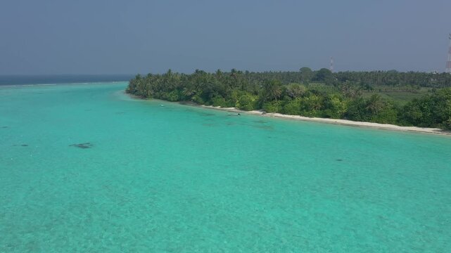 Aerial drone shot of Thoddoo island coastline featuring dense green palm forests, agricultural fields, a secluded white sand beach, and a small blue boat anchored in turquoise water.