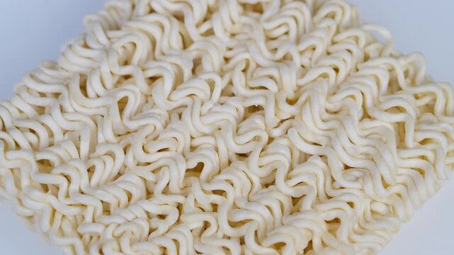 Closeup photograph capturing intricate surface of dehydrated noodles. Macro shot illustrating textured surface and pattern of dried instant noodles on white background