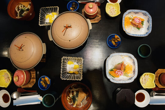 Traditional Japanese cuisine: nabe pots, soups, sashimi on dark table.