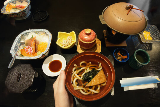 Traditional Japanese cuisine: nabe pots, soups, sashimi on dark table.