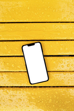 Phone with white blank screen on wet yellow bench after the rain
