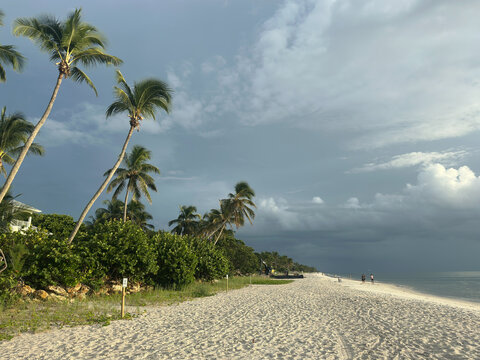Beach in Naples, FL with dark skies and people walking 