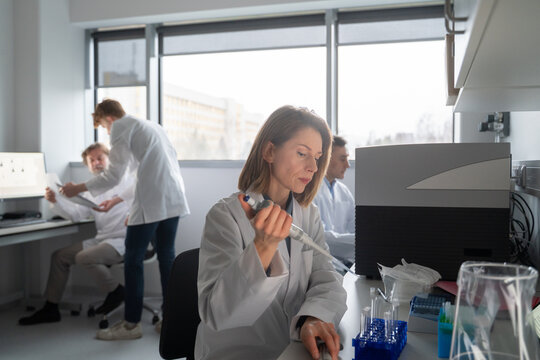 Scientist Uses Pipette in Lab While Colleagues Work Nearby