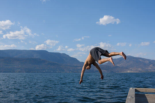 Man Jumps Into Water From Dock on Sunny Day Near Mountains