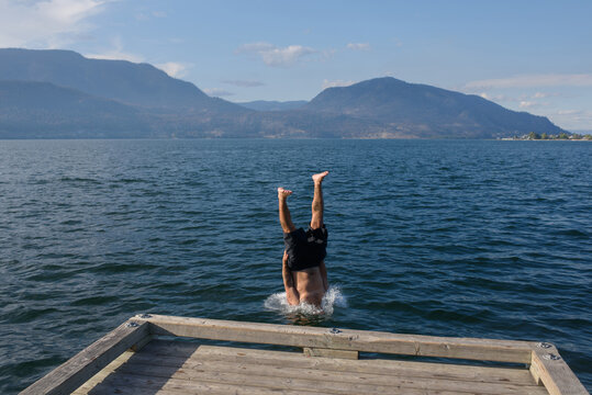 Person Performs a Head First Dive Into the Lake From a Wooden Dock