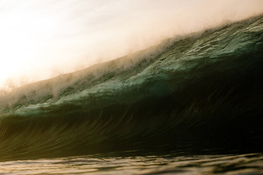 Massive ocean wave crashing under a bright sunset sky