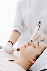 Naklejka premium Woman receiving professional facial microcurrent treatment at spa by aesthetician in white uniform