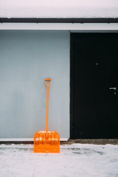 Snow shovel stands beside a door near a wall