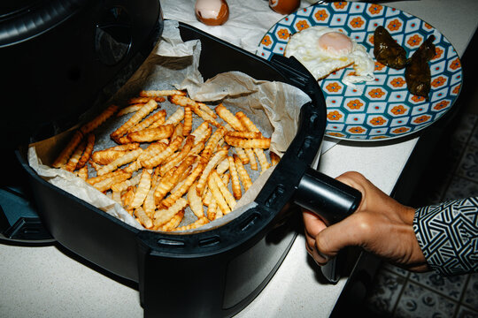 a man pulls out an air fryer basket with crinkle cut fries