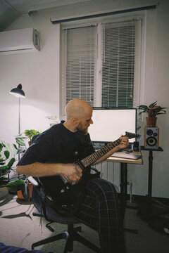 Bald man playing electric guitar in home studio