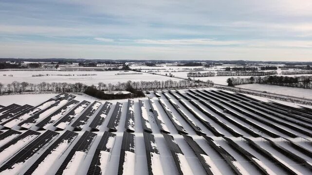 Winter aerial view of large snowy solar park with wind turbine in rural Danish landscape