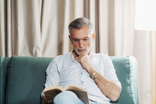 Senior man relaxing reading book on sofa