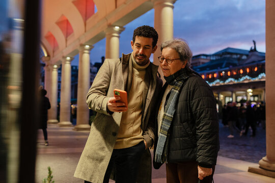 Son showing content on smartphone to his senior mother in a city